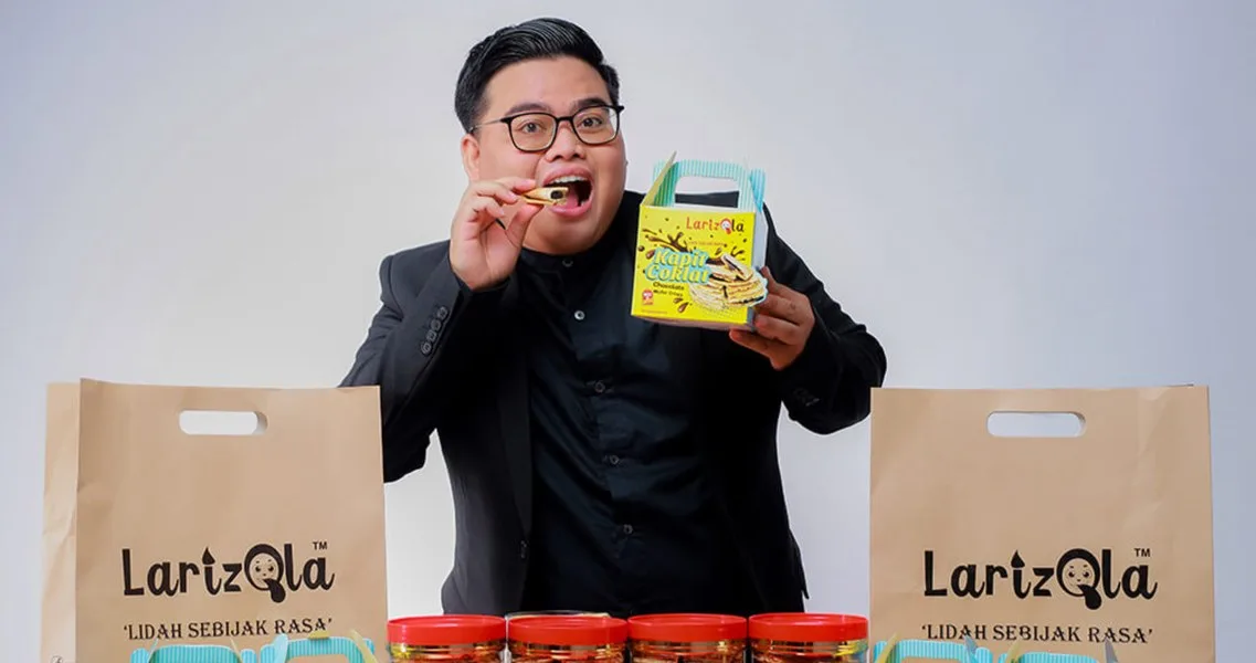 A food entrepreneur tasting his chocolate wafer product, surrounded by his branded packaging